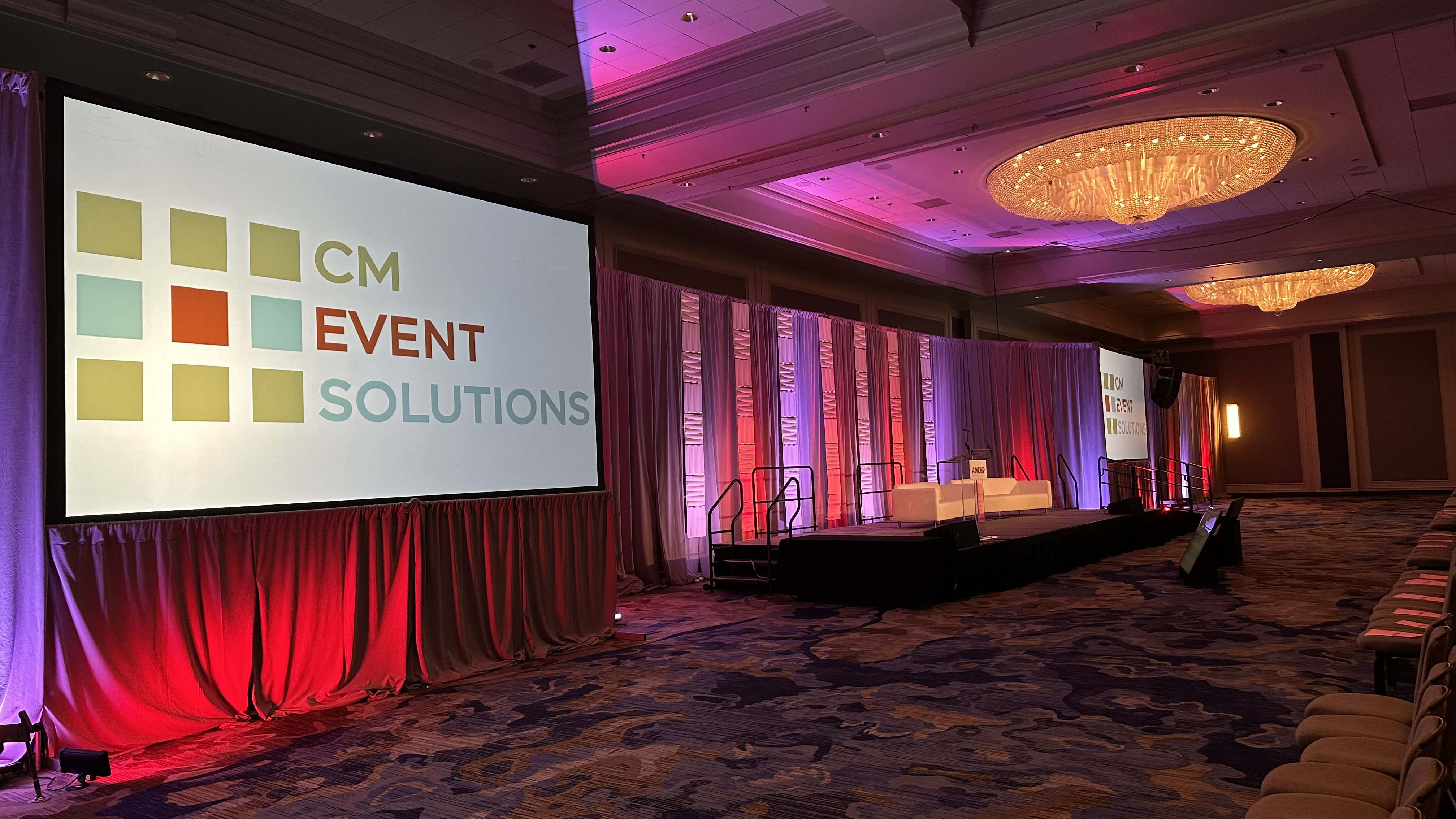 A room with an audience looking at four large screens